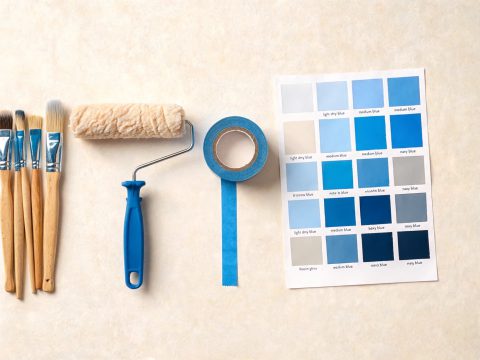 Brochas, rodillo, cinta de enmascarar y carta de colores azules sobre una mesa